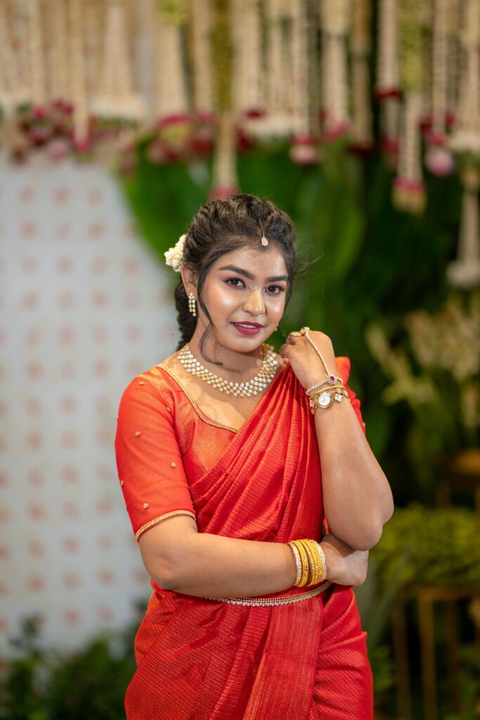 Woman in a traditional red sari with jewelry, smiling indoors. Perfect for cultural and fashion themes.